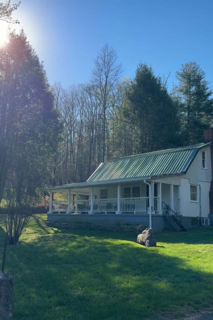 A landscape scene that features our Mountain Farm House property. The farm house is nestled between large trees with the morning sun shining in the background.